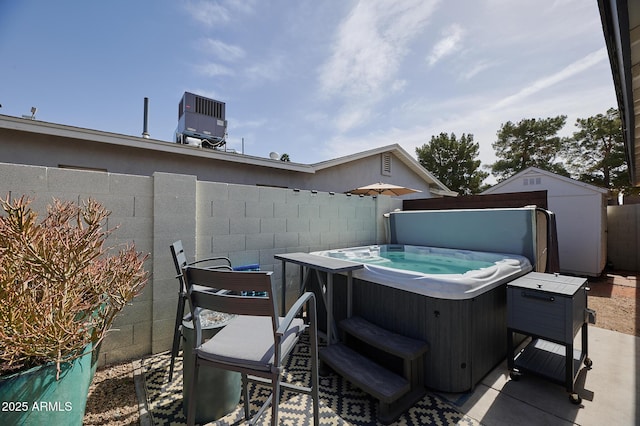 view of patio with a hot tub, central AC unit, a fenced backyard, an outbuilding, and a storage unit