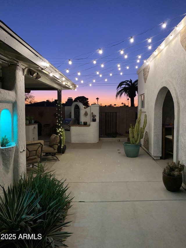 patio terrace at dusk featuring grilling area and fence