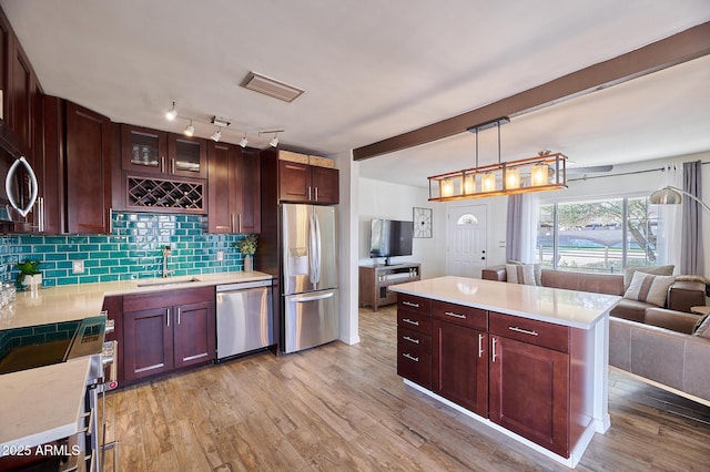 kitchen featuring appliances with stainless steel finishes, open floor plan, light countertops, light wood-style floors, and a sink