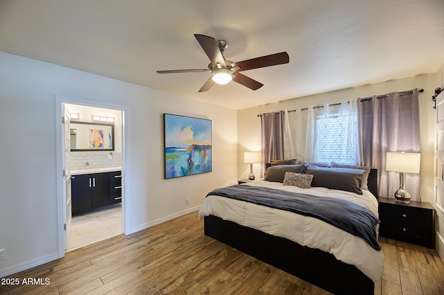 bedroom with connected bathroom, a sink, a ceiling fan, baseboards, and light wood-type flooring