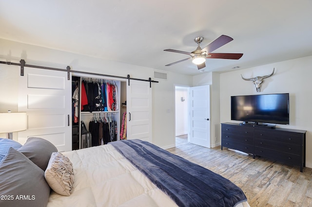 bedroom with a barn door, wood finished floors, visible vents, a ceiling fan, and a closet