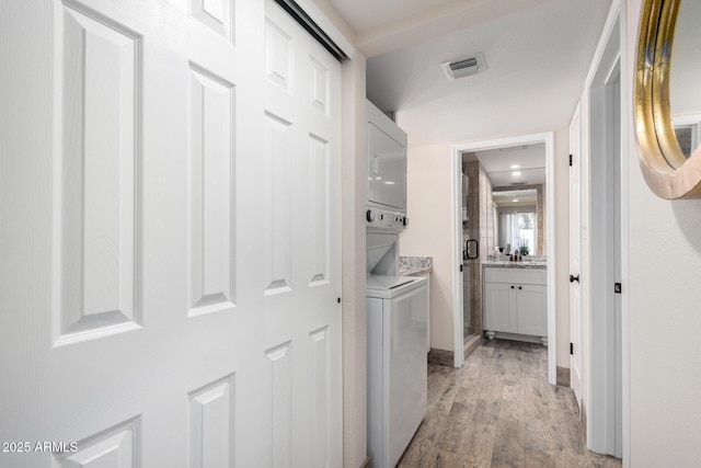 laundry area with stacked washer and dryer and light wood-type flooring