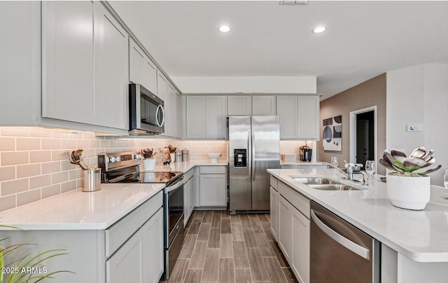 kitchen featuring stainless steel appliances, gray cabinets, decorative backsplash, and a sink