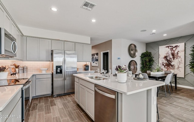 kitchen with appliances with stainless steel finishes, wood finish floors, a sink, light countertops, and gray cabinetry