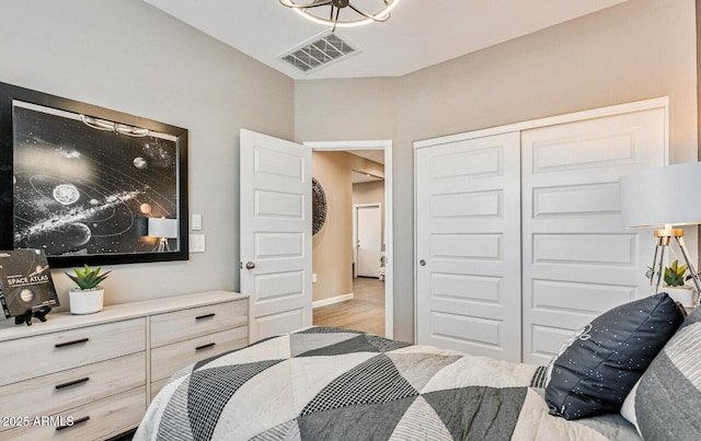 bedroom with visible vents, wood finished floors, an inviting chandelier, and a closet