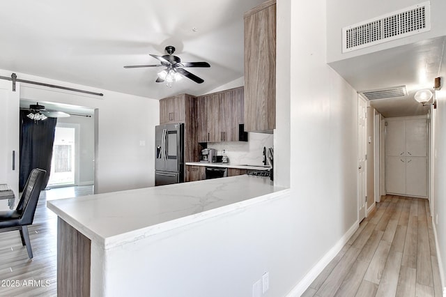 kitchen featuring light stone counters, a barn door, a ceiling fan, visible vents, and stainless steel fridge with ice dispenser