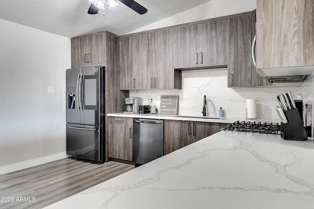 kitchen featuring lofted ceiling, a sink, appliances with stainless steel finishes, light wood-type flooring, and decorative backsplash