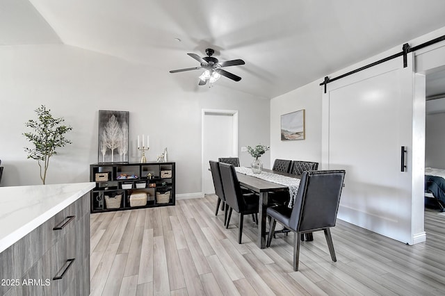 dining area with a barn door, light wood-style floors, vaulted ceiling, ceiling fan, and baseboards