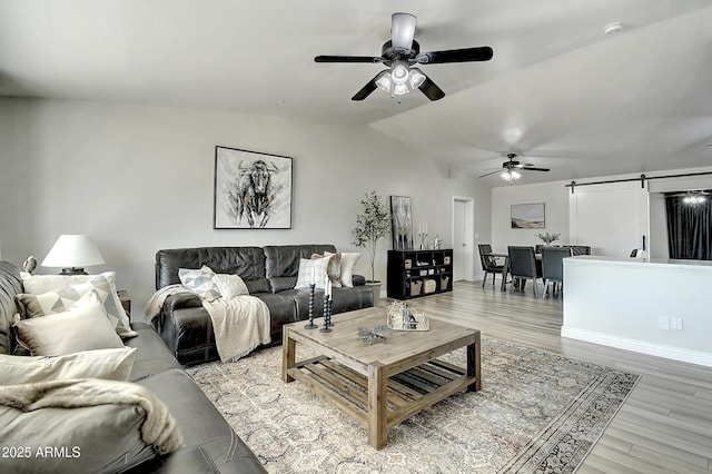 living area with vaulted ceiling, ceiling fan, a barn door, and wood finished floors