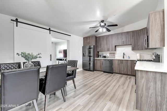 kitchen with a barn door, appliances with stainless steel finishes, light countertops, and backsplash