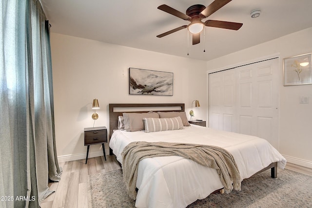 bedroom with ceiling fan, light wood finished floors, a closet, and baseboards