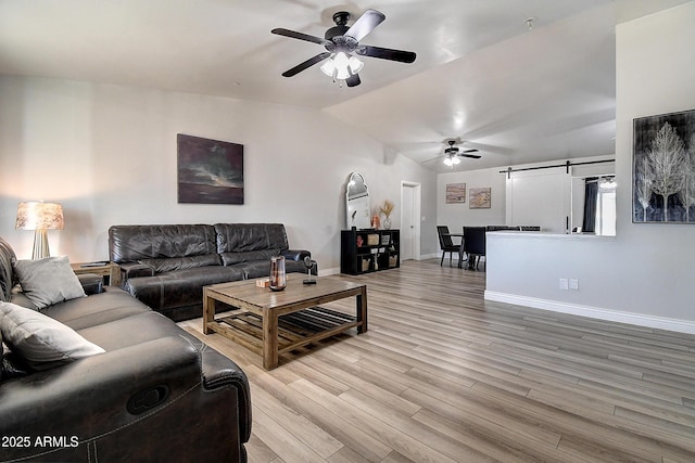 living area with a barn door, baseboards, a ceiling fan, vaulted ceiling, and light wood-style floors