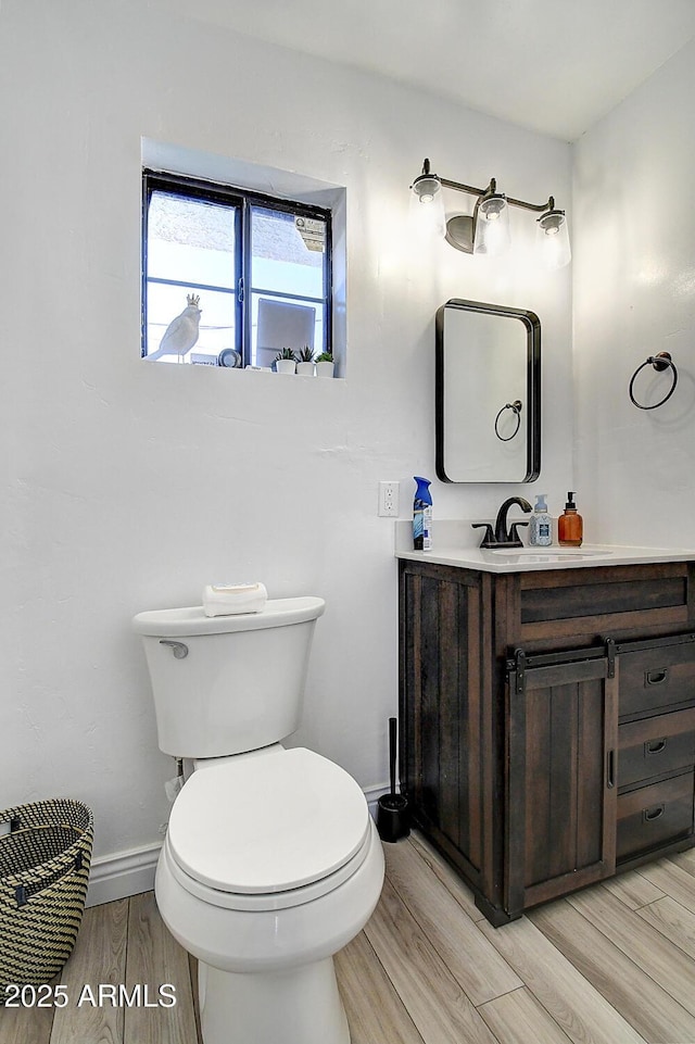 half bath with baseboards, vanity, toilet, and wood finished floors