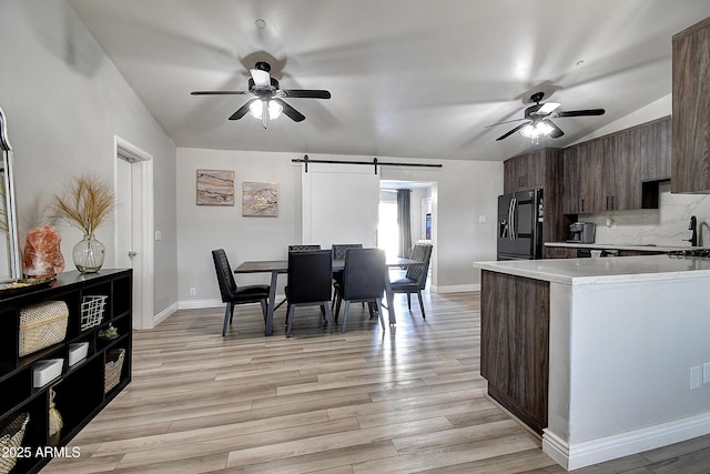 kitchen featuring ceiling fan, light countertops, a barn door, and refrigerator with ice dispenser