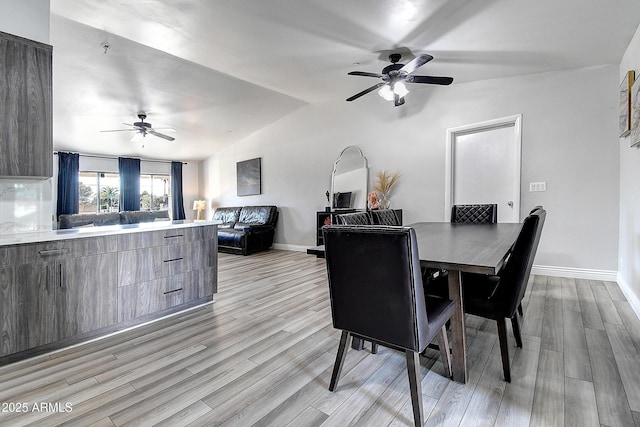 dining area with vaulted ceiling, ceiling fan, light wood-type flooring, and baseboards