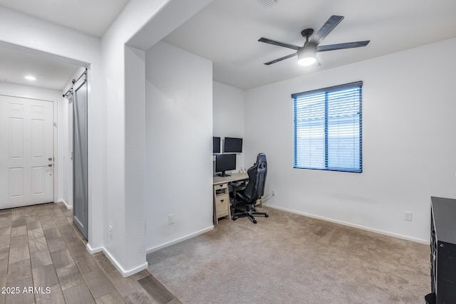 carpeted home office with a barn door and ceiling fan