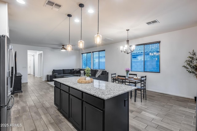 kitchen featuring ceiling fan with notable chandelier, pendant lighting, stainless steel refrigerator, a center island, and light stone counters