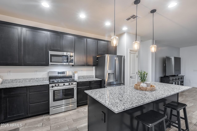 kitchen with pendant lighting, a breakfast bar area, stainless steel appliances, light stone countertops, and a kitchen island