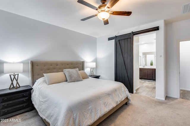 carpeted bedroom featuring a barn door, connected bathroom, and ceiling fan