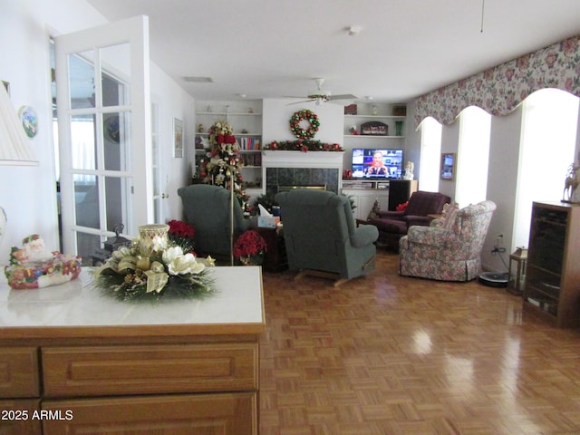 living room with a tiled fireplace, parquet flooring, and ceiling fan