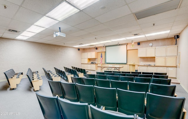 cinema featuring a paneled ceiling, visible vents, and a textured wall