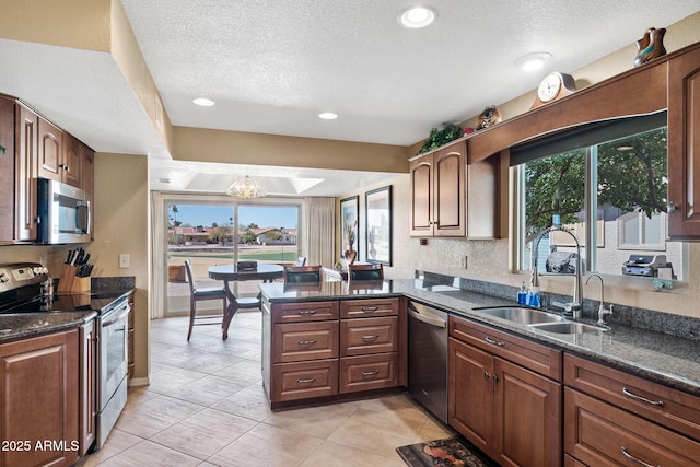 kitchen featuring dark stone counters, appliances with stainless steel finishes, a peninsula, a textured ceiling, and a sink