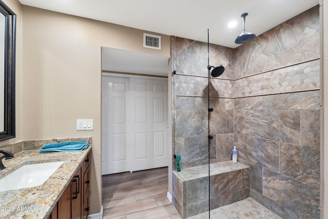 full bathroom with a textured wall, vanity, visible vents, wood tiled floor, and walk in shower