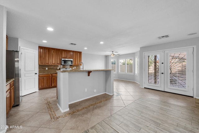 kitchen with a kitchen bar, decorative backsplash, stainless steel appliances, a kitchen island with sink, and ceiling fan