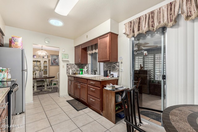 kitchen featuring electric stove, decorative light fixtures, backsplash, a sink, and ceiling fan with notable chandelier