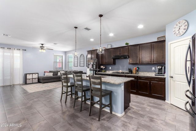 kitchen featuring decorative light fixtures, stainless steel fridge, a kitchen breakfast bar, a kitchen island with sink, and light stone counters