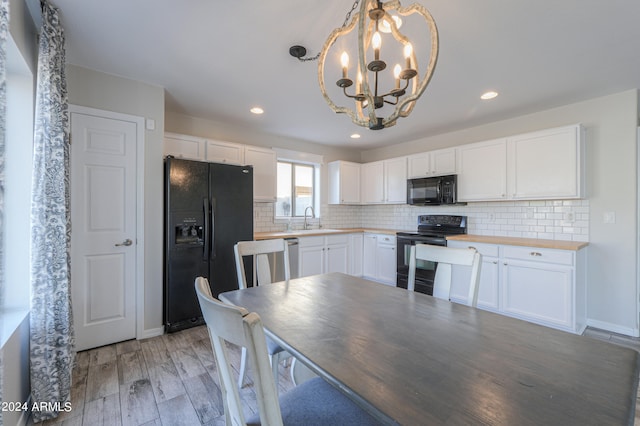 kitchen featuring white cabinetry, black appliances, light hardwood / wood-style flooring, decorative light fixtures, and a notable chandelier