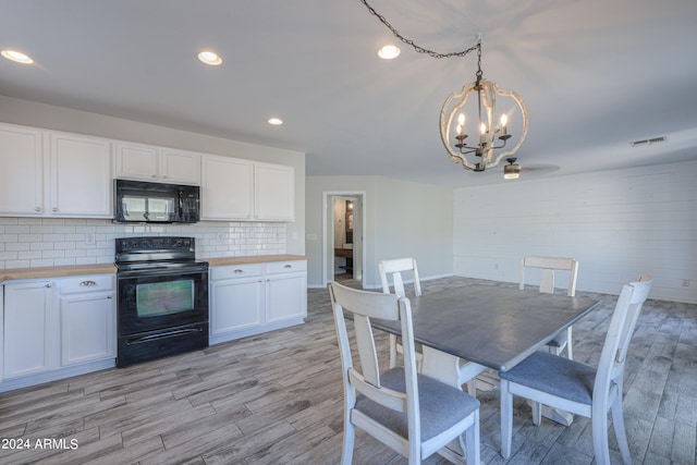 interior space with white cabinets, pendant lighting, light wood-type flooring, black appliances, and an inviting chandelier