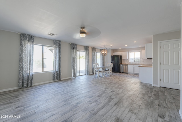 unfurnished living room with ceiling fan with notable chandelier, light hardwood / wood-style flooring, and a healthy amount of sunlight