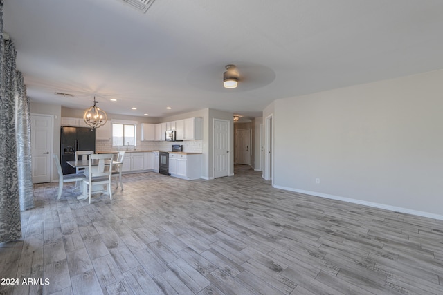 unfurnished living room featuring ceiling fan with notable chandelier and light wood-type flooring