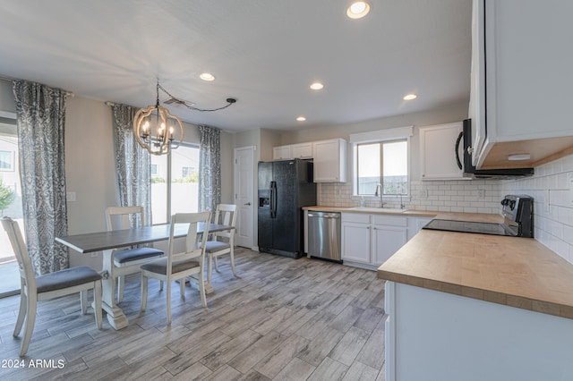 kitchen featuring hanging light fixtures, sink, black appliances, white cabinetry, and light wood-type flooring