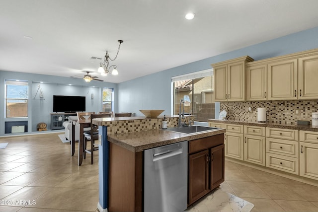 kitchen with decorative light fixtures, sink, stainless steel dishwasher, cream cabinets, and a center island with sink