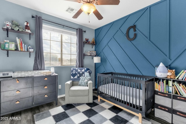 bedroom with a crib, ceiling fan, and dark hardwood / wood-style flooring