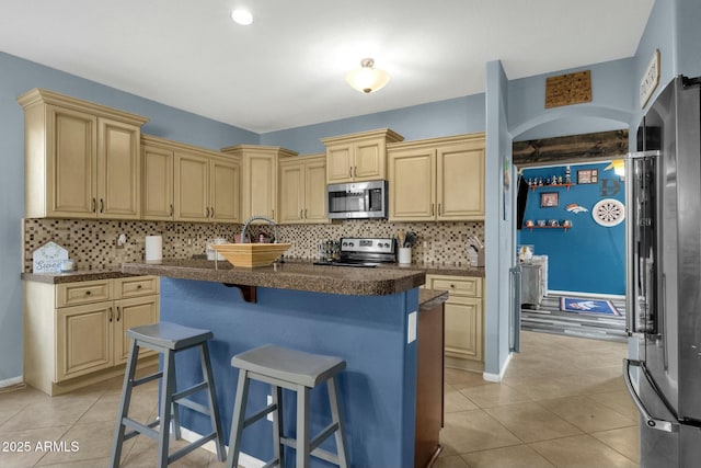 kitchen with light tile patterned flooring, stainless steel appliances, a kitchen bar, and tasteful backsplash