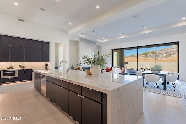 kitchen featuring light tile patterned flooring, appliances with stainless steel finishes, sink, decorative backsplash, and a large island with sink