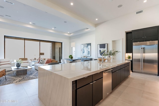 kitchen with stainless steel built in refrigerator, a kitchen island with sink, sink, and light tile patterned floors