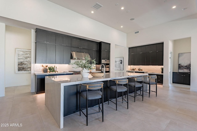 kitchen featuring a spacious island, a kitchen bar, light tile patterned floors, oven, and backsplash