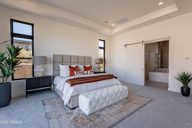 carpeted bedroom featuring a raised ceiling, ensuite bathroom, and a barn door