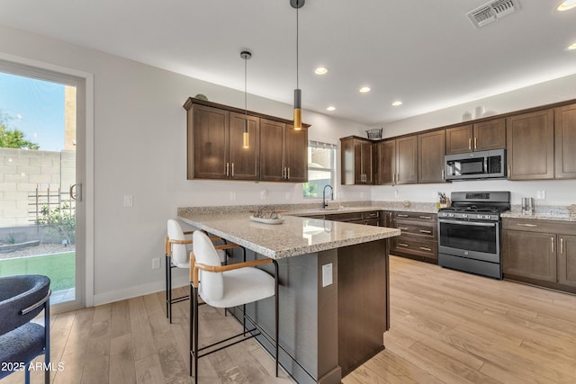 kitchen featuring stainless steel appliances, visible vents, dark brown cabinets, and light wood finished floors