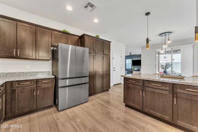 kitchen featuring light stone counters, dark brown cabinetry, visible vents, light wood-type flooring, and freestanding refrigerator