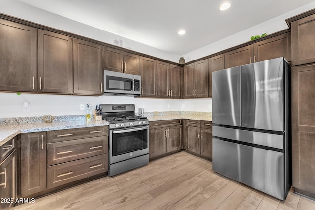 kitchen with light stone counters, recessed lighting, light wood-style flooring, appliances with stainless steel finishes, and dark brown cabinets