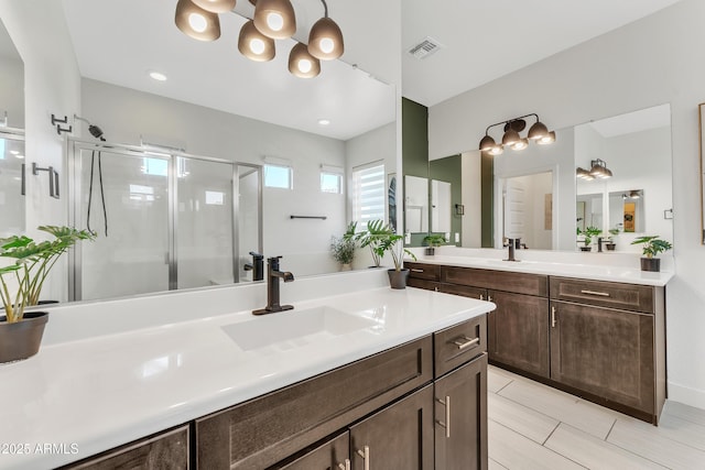 full bath with a stall shower, visible vents, two vanities, and a sink