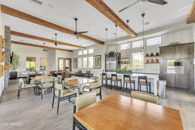 dining space with a ceiling fan, light wood-type flooring, and beamed ceiling