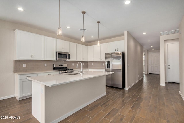 kitchen featuring appliances with stainless steel finishes, pendant lighting, an island with sink, sink, and white cabinets