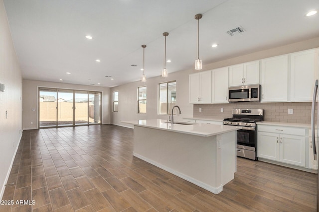 kitchen with sink, a center island with sink, pendant lighting, stainless steel appliances, and white cabinets