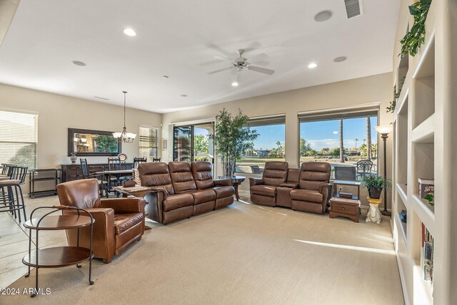 carpeted living room with ceiling fan with notable chandelier